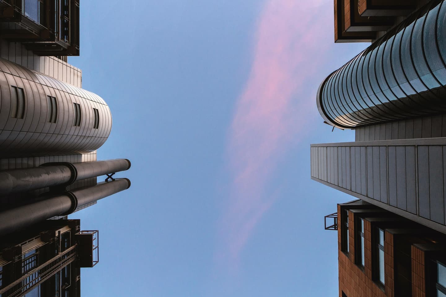 Looking up at modern curved architecture buildings against a blue sky with pink clouds at dusk.