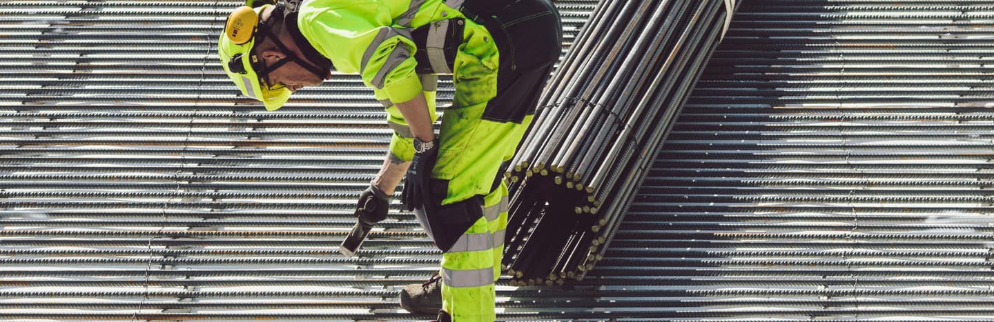 Construction worker in high-visibility clothing working with metal rebar on a construction site.