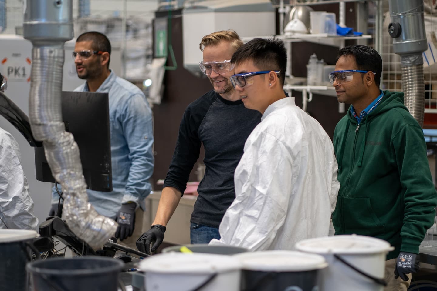 Men with safety goggles looking on interestingly at a piece of manufacturing equipment in progress in a factory setup.