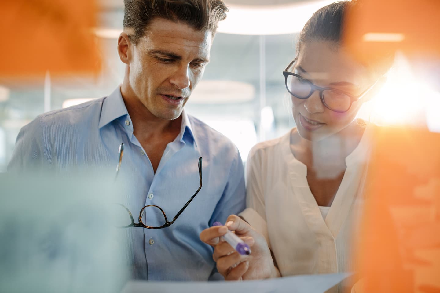 Two professionals in an office reviewing documents together, with warm orange light filtering through the glass.