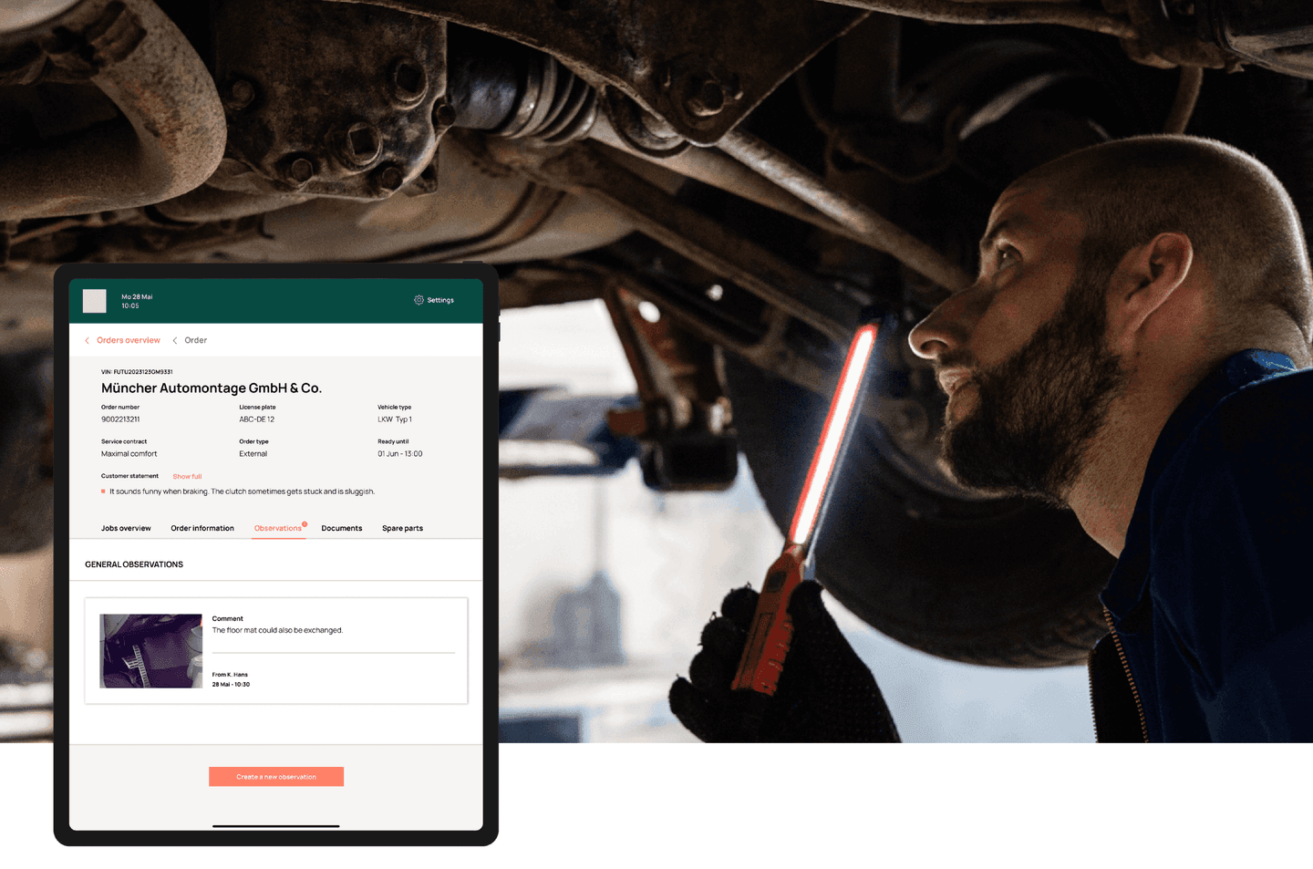 Mechanic inspecting car undercarriage with work light while viewing repair order details on tablet screen.