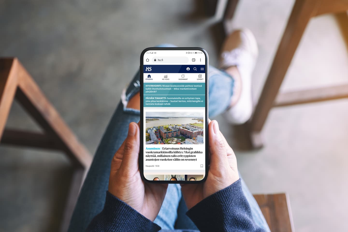 Person holding smartphone displaying Finnish news website HS.fi with article about housing in Helsinki.